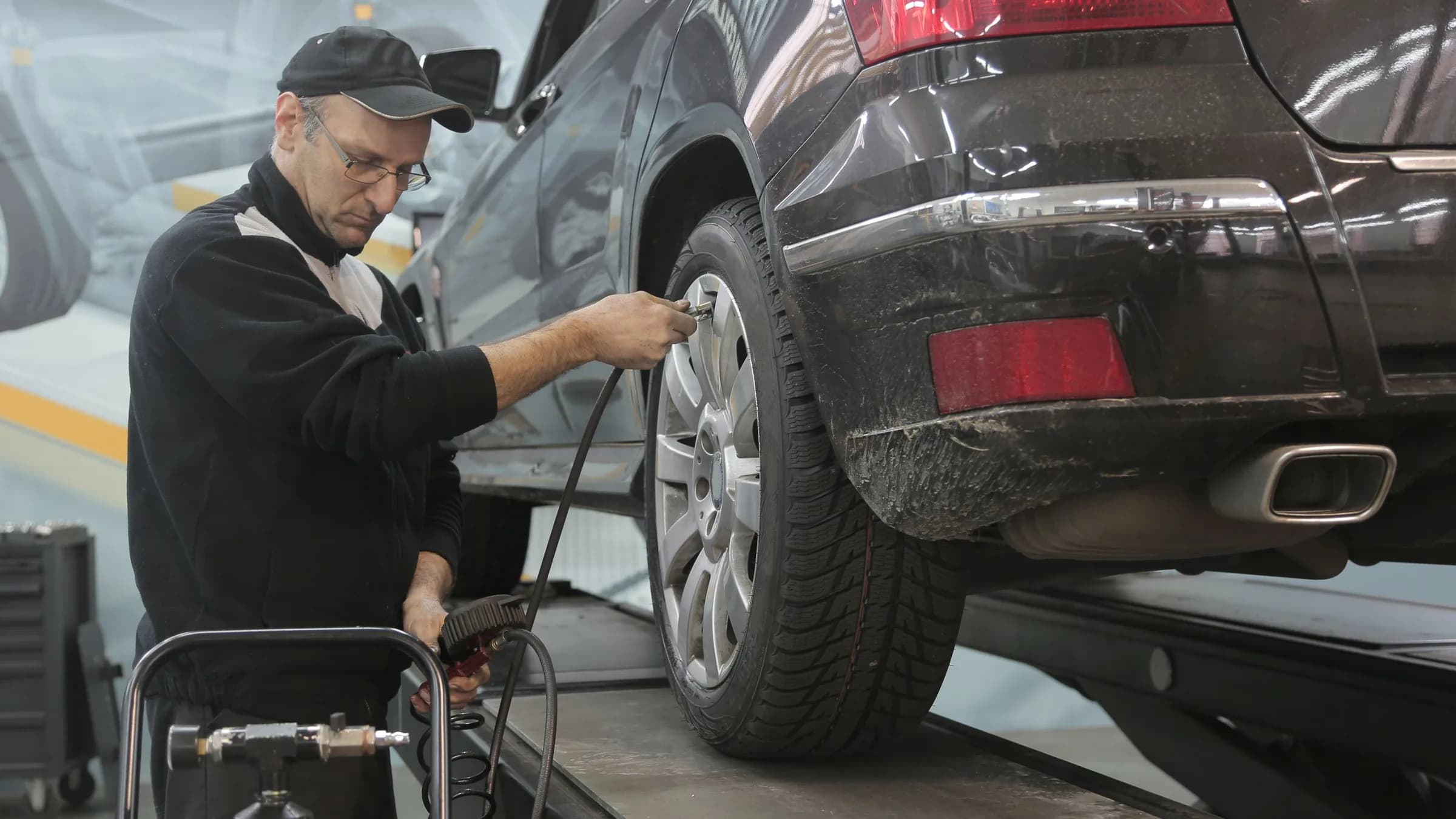 A mechanic checks the tyre pressure on a car raised on a workshop lift.